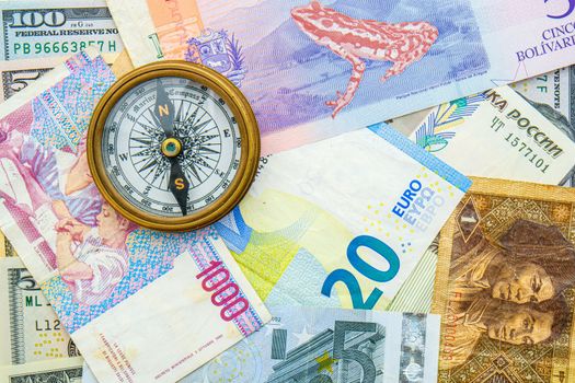 Top view of world currencies including Euros, US dollars, Russian, Chinese with a compass laid on top, concept of travelling, exploration. High quality photo