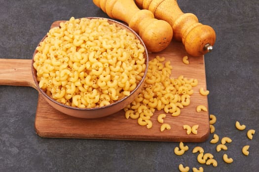 Elbow macaroni in bowl on black background