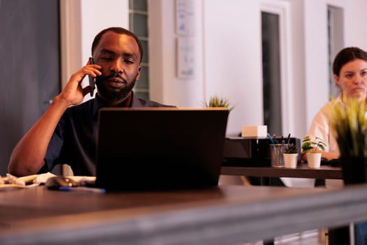 Project manager discussing business plan on smartphone, african american man answering client mobile call. Corporate worker having telephone conversation in coworking space at night