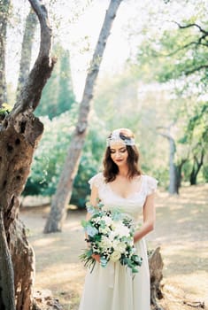 Bride with a bouquet of roses stands near a tree in the park. High quality photo