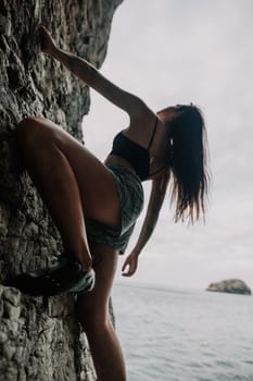 A girl climbs a rock. The athlete trains in nature. Woman overcomes difficult climbing route. Extreme hobby. Tourist woman rock climber hiking on mountains rocks over beautiful sea coast