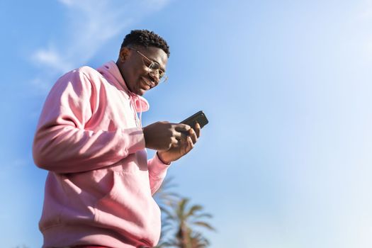 Low angle view of African American man using smart phone outdoors. Copy space Lifestyle concept.