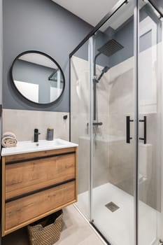 Bathroom with a washbasin on a floating vanity. On a gray wall is a round mirror in a black metal frame. Bathroom is filled with a fashionable design solution, pleasant and comfortable little things