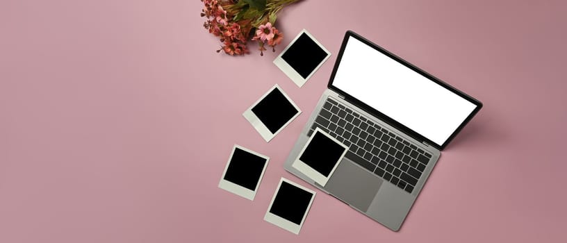 Laptop computer with white screen, blank photo frames and beautiful blooming flower bouquet on pink background.