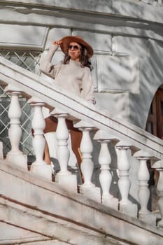 Woman walks in the city, lifestyle. Young beautiful woman in a loose light sweater, brown skirt and sneakers with a hat