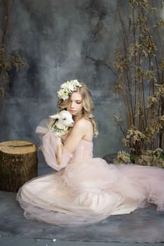 A young blonde woman in an airy pink dress with a white kid. Spring portrait of a woman