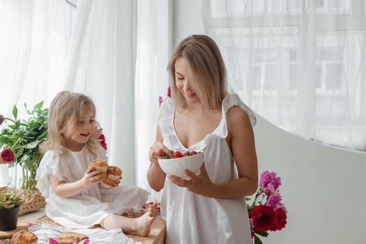 A little blonde girl with her mom on a kitchen countertop decorated with peonies. The concept of the relationship between mother and daughter. Spring atmosphere