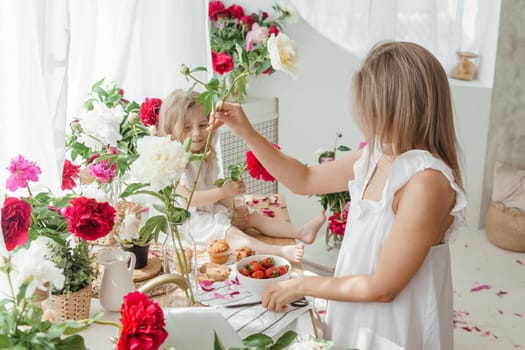 A little blonde girl with her mom on a kitchen countertop decorated with peonies. The concept of the relationship between mother and daughter. Spring atmosphere.