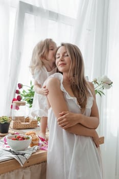 A little blonde girl with her mom on a kitchen countertop decorated with peonies. The concept of the relationship between mother and daughter. Spring atmosphere.