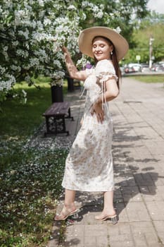 An attractive long-haired woman walks in the spring in the park of blooming apple trees. Spring portrait of a woman