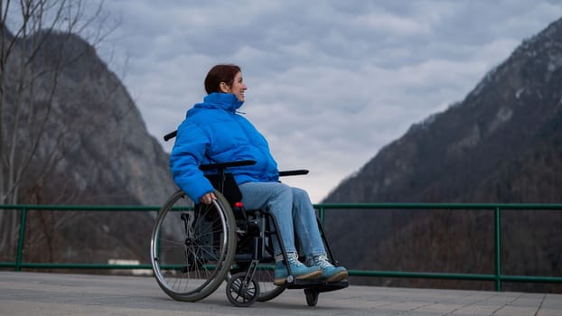 A woman in a wheelchair on a point view admires the high mountains. Thrust to life