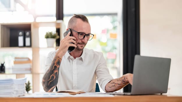 Handsome mature businessman is talking on the mobile phone and smiling while working in office..