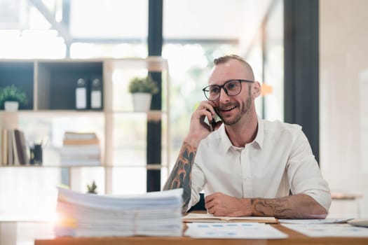 Handsome mature businessman is talking on the mobile phone and smiling while working in office..