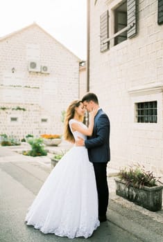 Groom hugs bride near the old stone house on the street. High quality photo