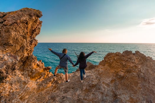 The tourist, standing with her hands raised, reaches the edge of the earth and sees a rock. The girl welcomes the sun. Design concept. A successful woman looks at the sunset with open arms