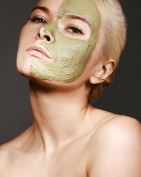 Beautiful Woman Applying Green Facial Mask. Beauty Treatments. Close-up Portrait of Spa Girl Apply Clay Facial mask on grey background.