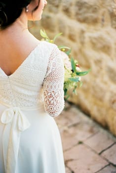 Bride in a lace dress with a bouquet in the courtyard of the house. Back view. Cropped. High quality photo