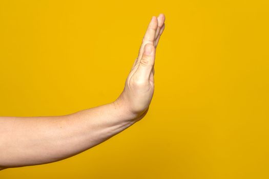 Hand of strong man making stop gesture to eliminate adversities and misfortunes isolated on yellow studio background