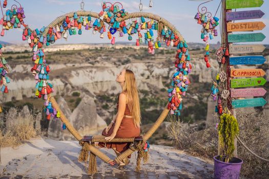 Young woman exploring valley with rock formations and fairy caves near Goreme in Cappadocia Turkey. Wish tree. Small multi-colored jugs with inscriptions, wishes hanging on the branches of a tree., against the backdrop of sand ruins and blue sky.