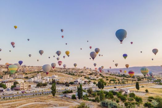 Colorful hot air balloons flying over at fairy chimneys valley in Nevsehir, Goreme, Cappadocia Turkey. Spectacular panoramic drone view of the underground city and ballooning tourism. High quality.