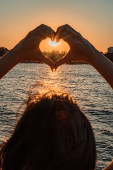 Silhouette against the sunset - hands folded in the shape of a heart. Sun with rays between the palms. Concept for Valentine's Day, declaration of love. Minimalism, space for text, warm colors