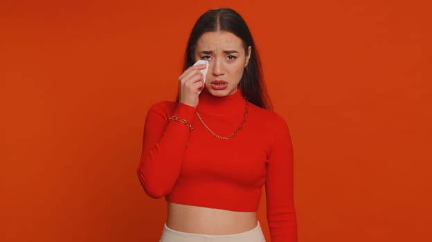 Upset disappointed pretty young woman in crop top wipes tears and cries from despair being sad because of unfair things. Millennial girl in depression, despair, loss isolated on red studio background