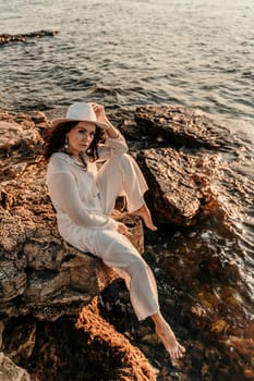 A woman in a white pantsuit and hat is standing on the beach enjoying the sea. Happy summer holidays.