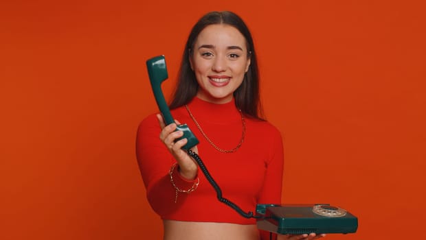 Hey you, call me back. Pretty young woman in crop top talking on wired vintage old-fashioned retro telephone of 80s, says hey you call me back. Girl working in call center isolated on red background