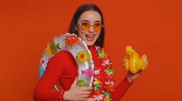 Traveler tourist young woman celebrating, dancing fooling with swimming inflatable duck toy. Concept summer vacation, journey, trip to seaside. Lovely girl in sunglasses on red studio background