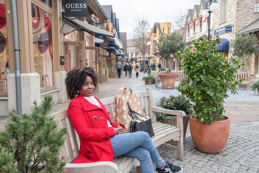 beautiful african american woman with big shopping bags relaxing after shopping on outdoor bench, Maasmechelen,Belgium,February 17,2023, High quality photo