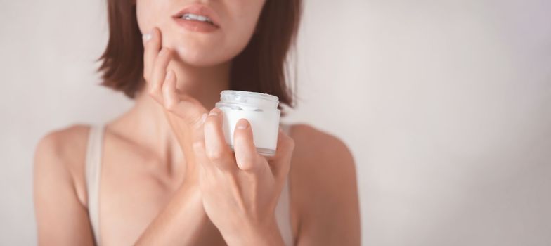 A young girl holds a jar of cream in her hands, applies a moisturizing balm to the body and face, takes care of beauty and health, close-up.