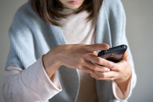 A young well-groomed woman holds a smartphone in her hands, communicates with colleagues, friends, a girl in a casual sweater works online using her mobile device.