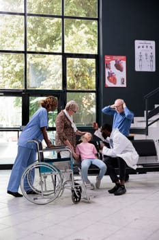 Grandparents being scared after exhausted granddaughter falling down on chair in hospital waiting area during appointment. Doctor consulting unconscious little child before putting medical expertise