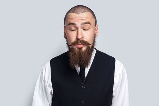 Portrait of shy flirting man with beard and mustache standing with closed eyes, sending air kisses, demonstrating his romantic feelings. Indoor studio shot isolated on gray background.