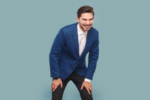 Portrait of smiling cunning man with mustache standing and laughing happily, looking at camera, wearing official style suit. Indoor studio shot isolated on light blue background.