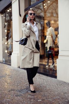 Stylish european woman in sunglasses is talking phone on city street background. High quality photo