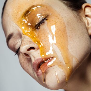 Closeup profile portrait of relaxed calm young brunette woman with freckles, standing with closed eyes, doing skin care procedures with honey mask. Indoor studio shot isolated on gray background.