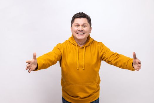 Free hugs. Portrait of friendly kind man stretching hands to camera and smiling broadly, going to embrace, share love, wearing urban style hoodie. Indoor studio shot isolated on white background.