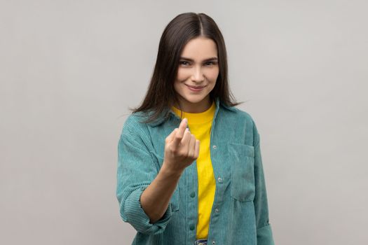 Come here. Portrait of attractive woman gesturing come to me, beckoning with finger, inviting for confidential talk, wearing casual style jacket. Indoor studio shot isolated on gray background.