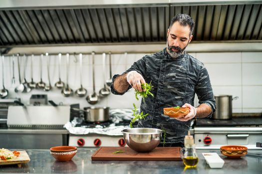 Professional cook is preparing meal in restaurant's kitchen. He is making salad.