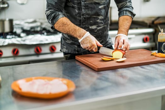 Professional cook is preparing meal in restaurant's kitchen. He is cutting apples.