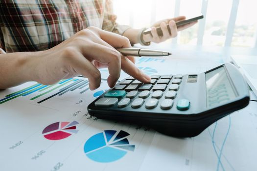 Close up of businessman or accountant hand holding pencil working on calculator to calculate financial data report, accountancy document and laptop computer at office, business concept.