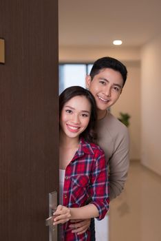 Cheerful young asian couple inviting people to enter in home