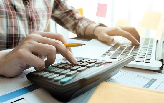 Business woman working in finance and accounting Analyze financial budget with calculator and laptop computer in the office.