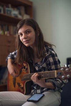 Teenage girl is playing guitar at home.