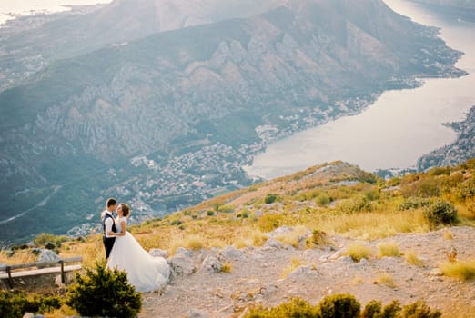 Groom hugs bride on Mount Lovcen near the bench against the backdrop of the Kotor Bay. Montenegro. High quality photo