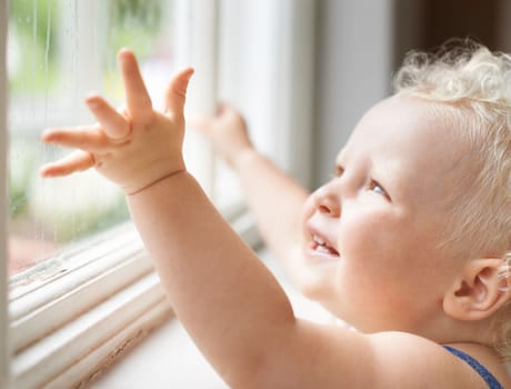 Gazing in wonder at the world. A cute little toddler looking through a window in wonder