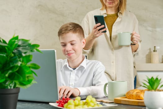 Happy mother and son have healthy breakfast in the kitchen at home. Happy mother and son in the kitchen. breakfast and digital devices Concept of happy family and healthy food.