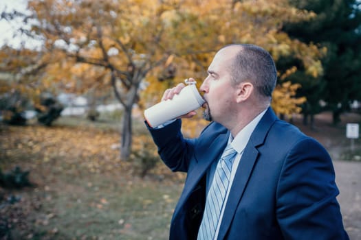 Mature entrepreneur drink coffee in autumn park. Senior executive rest in city park.