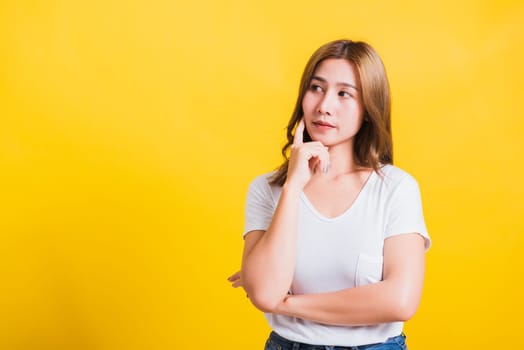 Portrait Asian Thai beautiful young woman wearing white t-shirt standing chin handle relaxed thinking about something about the question studio shot, isolated on yellow background with copy space